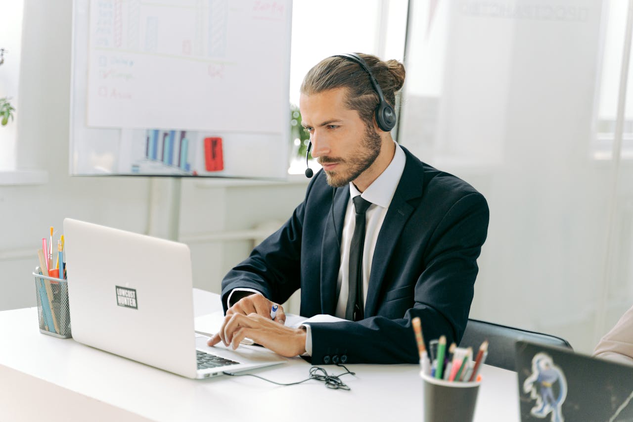 Employee in a suit working at a call center, focused on his laptop with a headset.